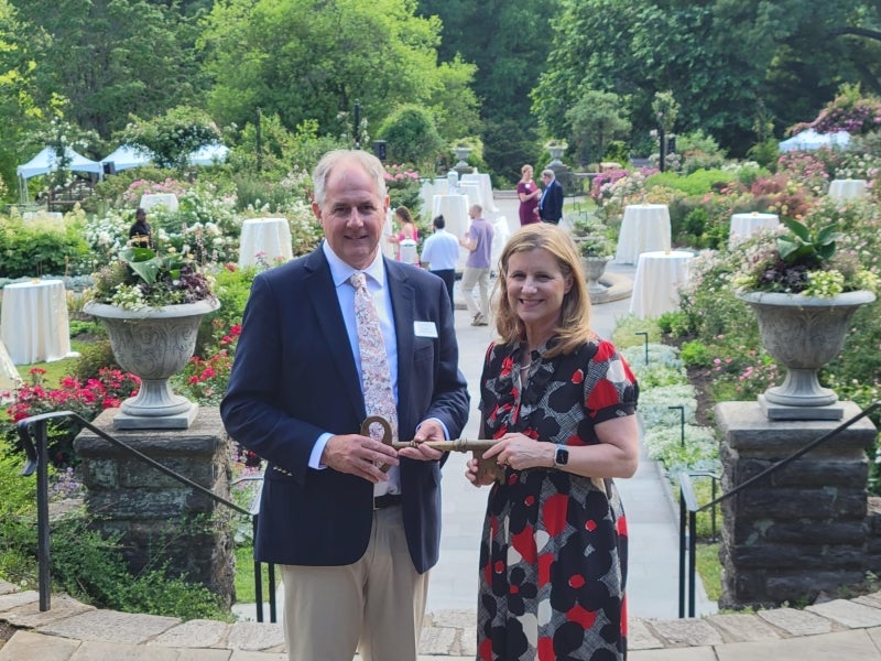 A man and a woman hold a large, historic key in a rose garden gala. 