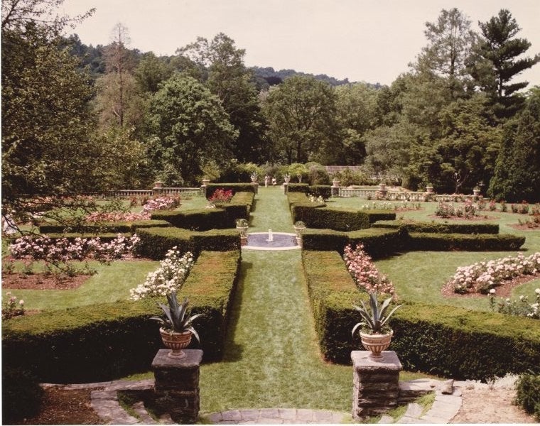 A rose garden with manicured hedges and grass paths. 