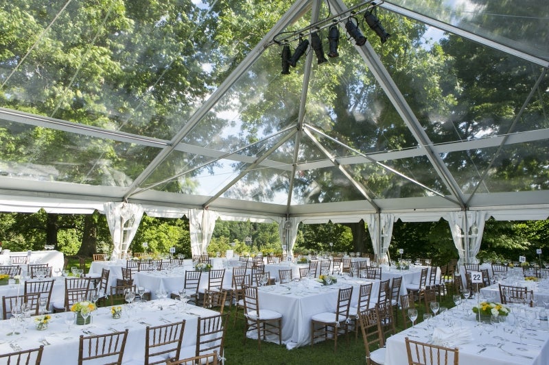 A clear-top wedding reception tent outside and surrounded by trees. 
