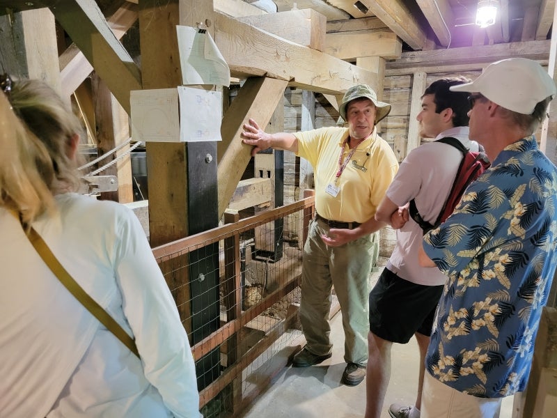 A man in a yellow shirt and bucket hat talks to a group of people.