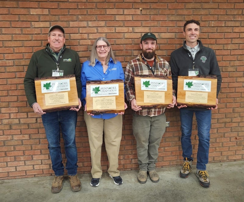 Four people stand against a brick wall holding awards.