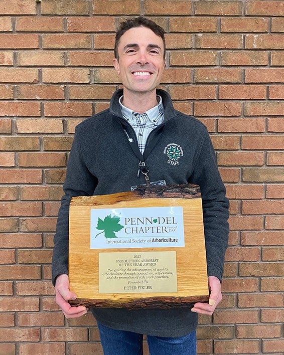 A man stands smiling in front of a brick wall holding an award.