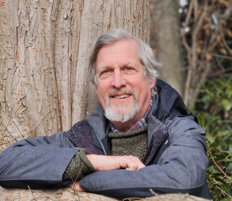 Smiling man with white hair and beard wearing a gray hooded jacket