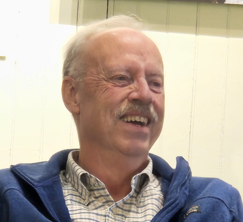 Smiling man with white hair wearing a blue zip-up sweater