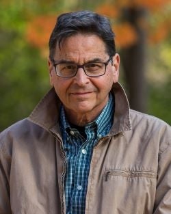 White man with dark hair wearing glasses and a light brown jacket