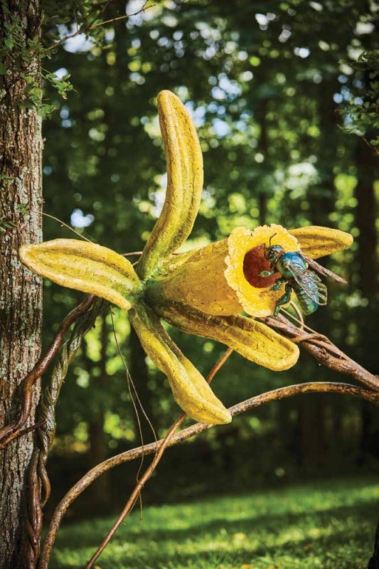 A large, fabricated yellow flower and bee outdoors. 