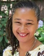 A headshot of a smiling black woman wearing a floral shirt outdoors.