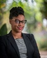 Headshot of a black woman outdoors wearing cateye glasses, a black-and-white striped shirt, and a black blazer.