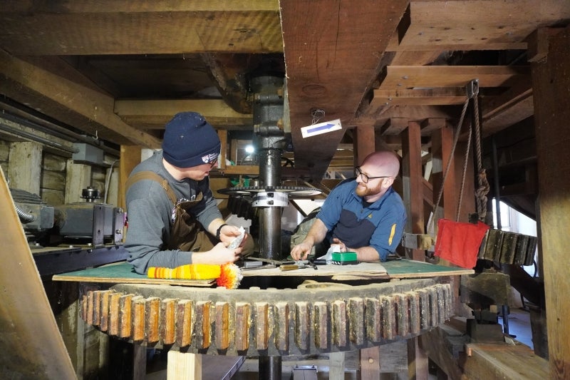 Two men lying on a big gear inside a mill