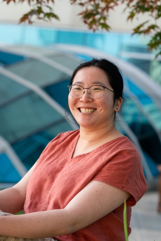 Smiling Asian woman wearing a blush-orange short-sleeve shirt.
