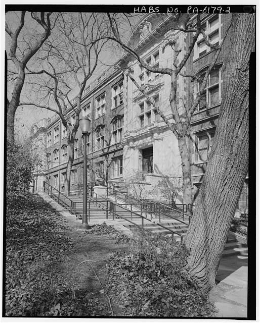 A black-and-white photograph of a long set of outdoor stairs lined with trees in front of a building on a college campus.