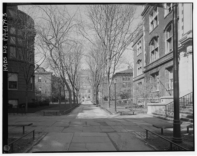 A black-and-white photograph of a walkway on a college campus lined with trees and buildings.