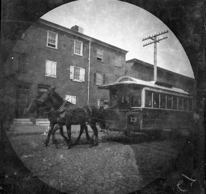 A black-and-white photograph from the late 1800s of a horse-drawn trolley car on a city street.