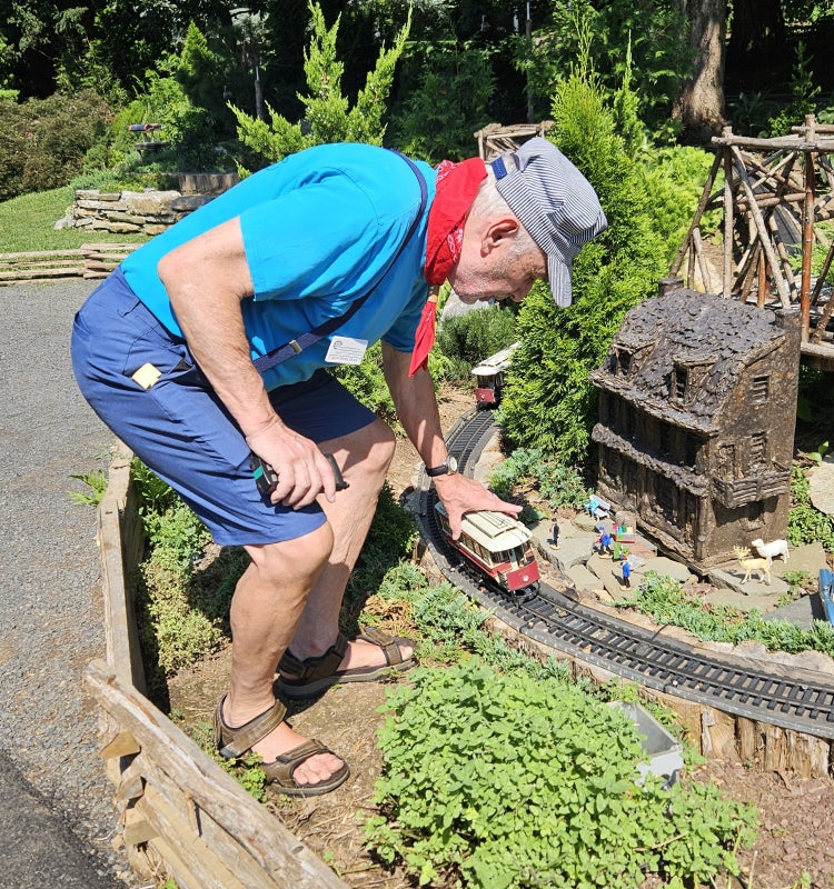 Man in train engineer hat and red bandanna places a train car on a track