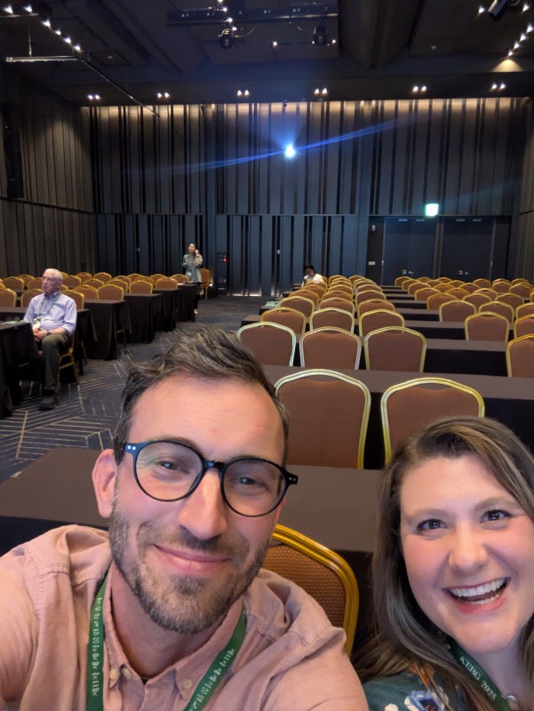 A man and woman take a selfie in an auditorium smiling into the camera. 