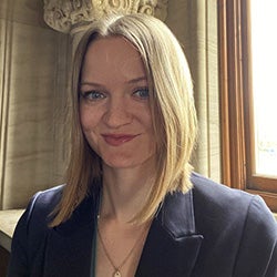 A headshot of a blonde woman smiling at the camera wearing a navy blazer. 