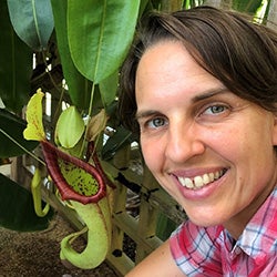 A head shot of a woman smiling and posed near a plant. 