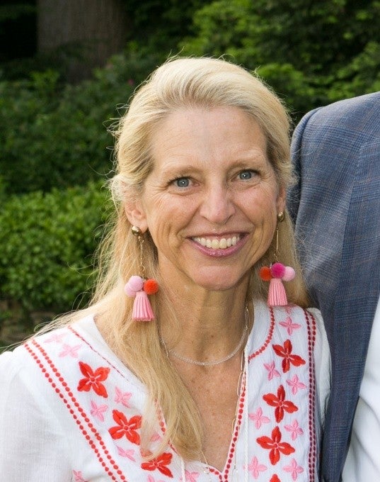 Woman with long blonde hair in a white top with pink and red trim