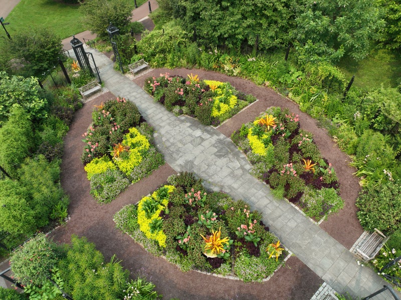 An aerial view of a symmetrical garden shaped like an oval with four garden beds divided by a cross-shaped path. 