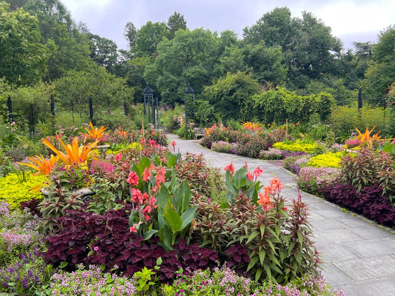 A garden filled with bright pink, orange, lime green, and deep purple flowers and plants with a paved pathway through the middle. 